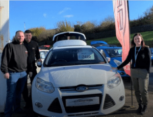 Image shows the team from CARS standing around a car with a person from St Richards Hospice charity