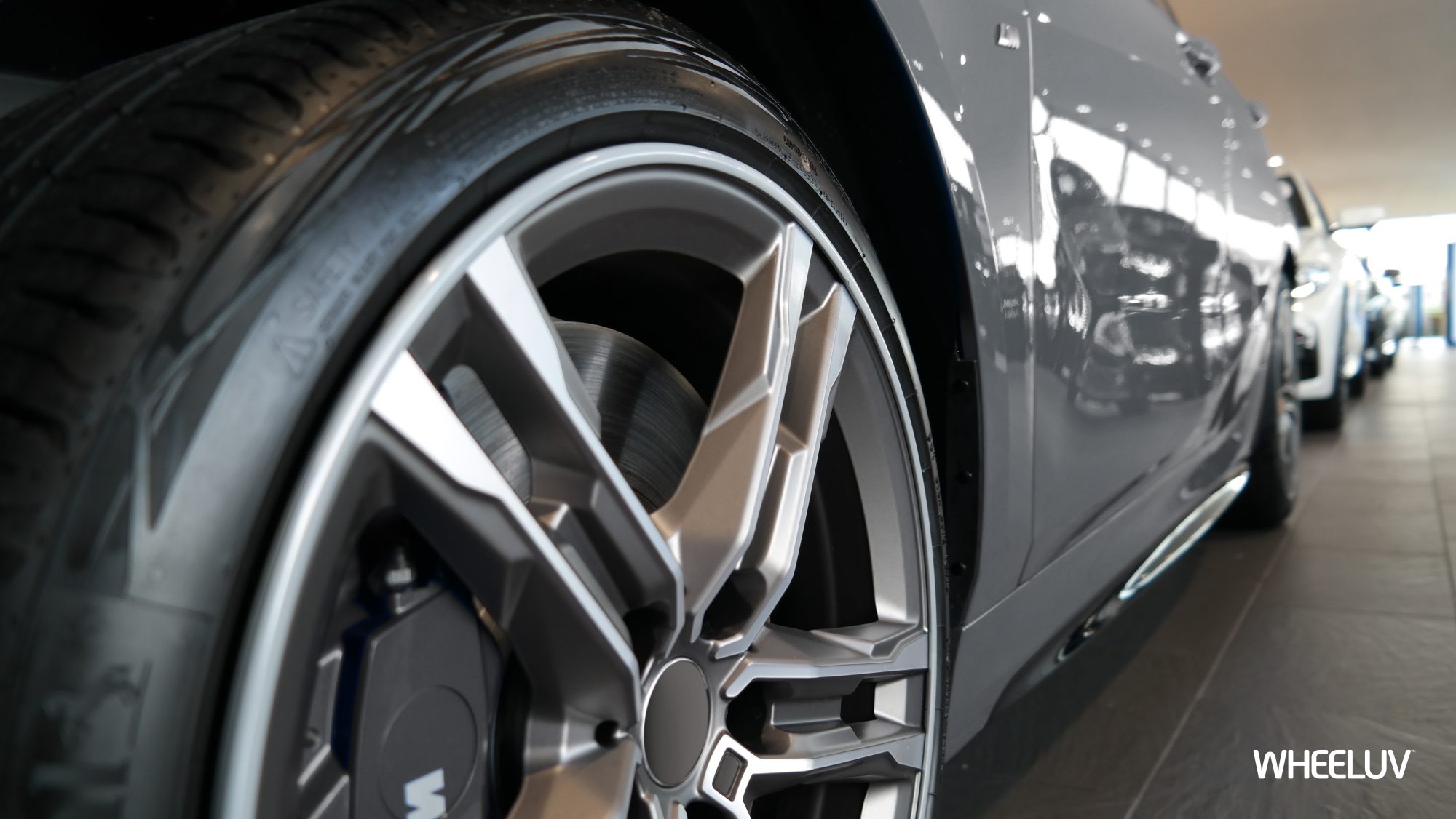 The photo shows a close up of an alloy wheel on a grey car in a showroom